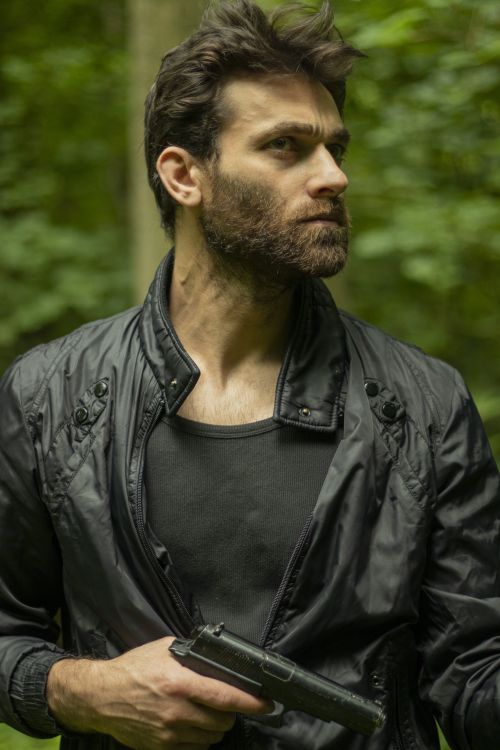 Free Portrait of a bearded man in a black jacket holding a pistol outdoors. Stock Photo