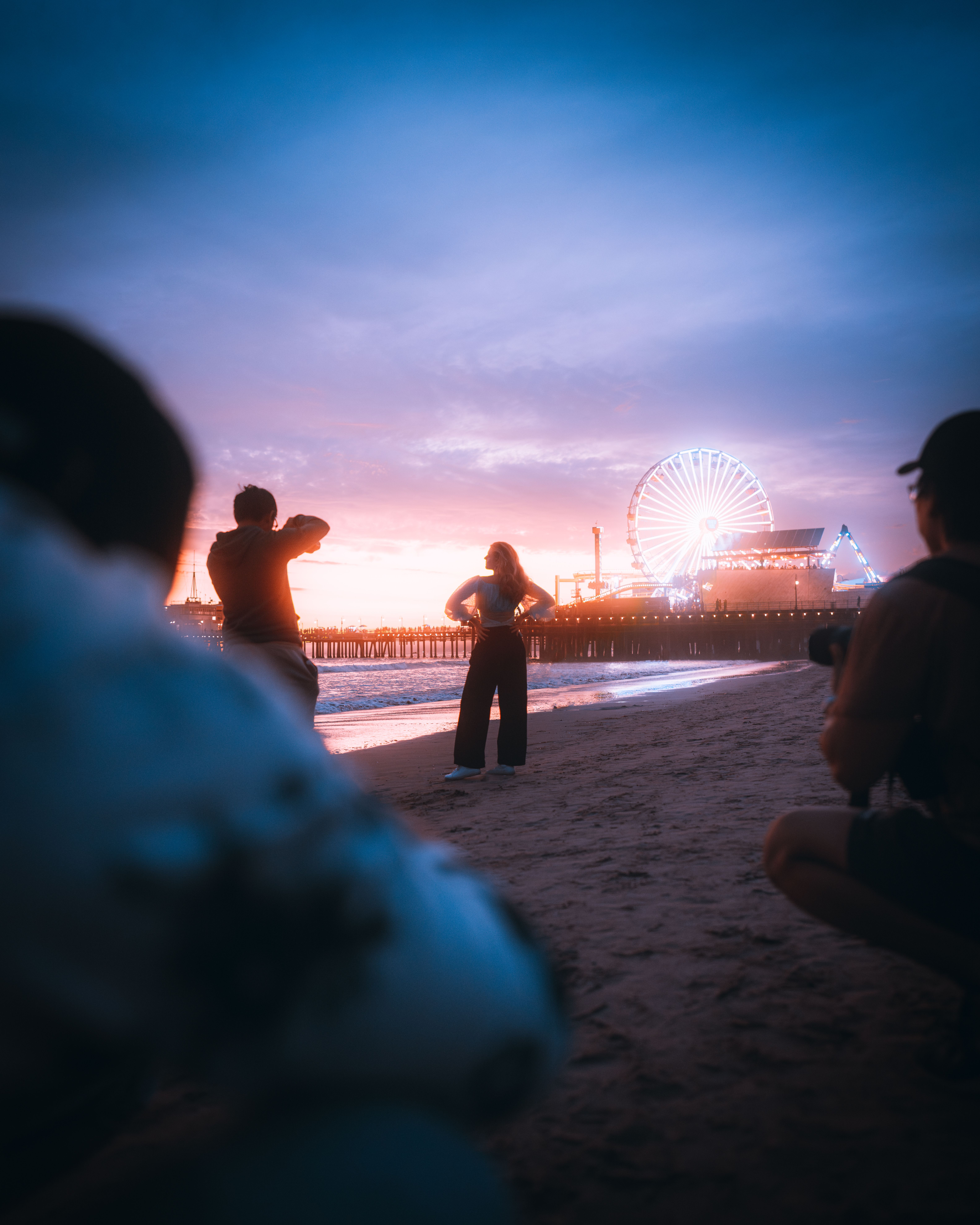 Dramatic beach photo shoot at sunset with Santa Monica Pier and Ferris wheel in background.
