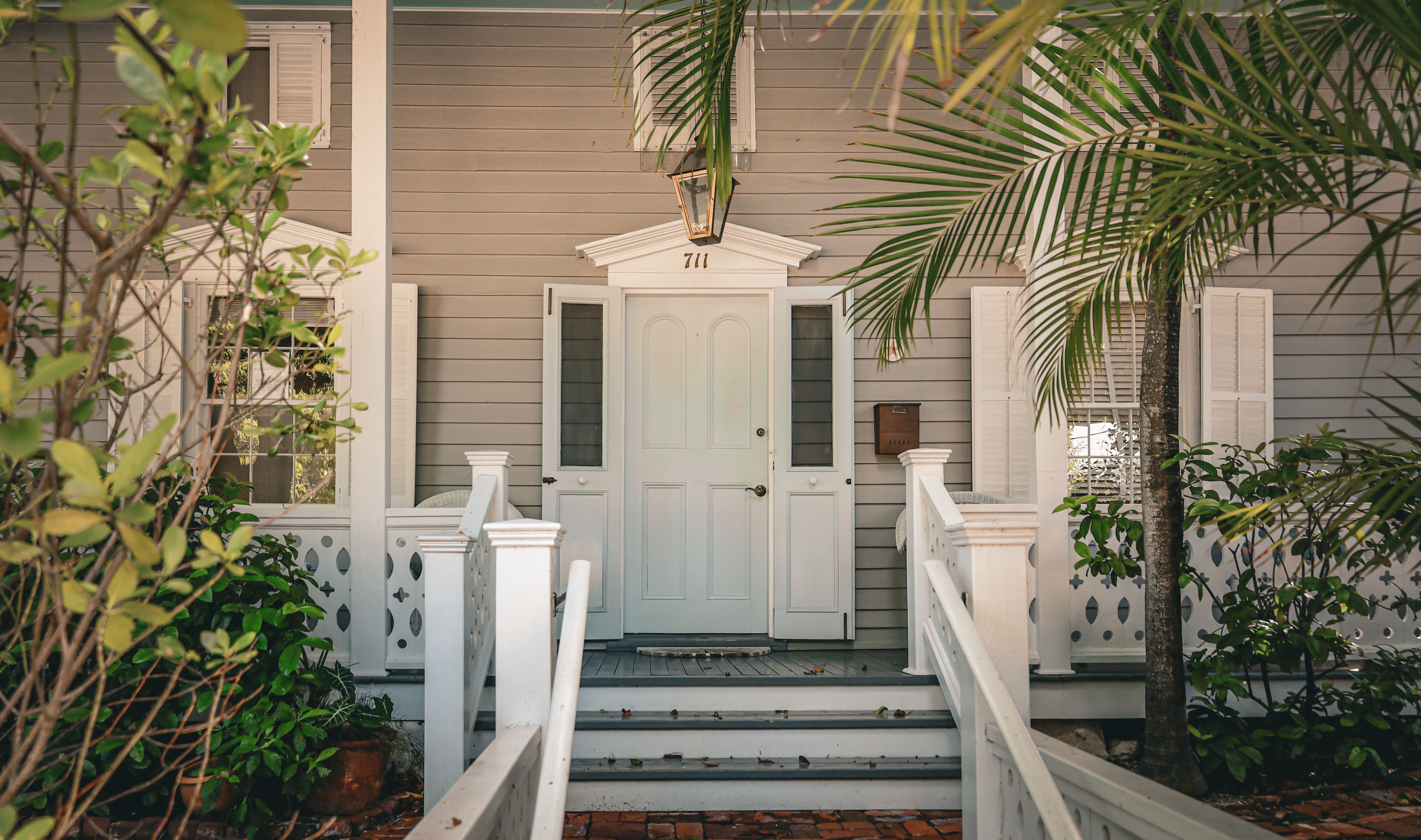 Charming white porch entrance surrounded by tropical foliage on a sunny day. — photo by Arian Fernandez