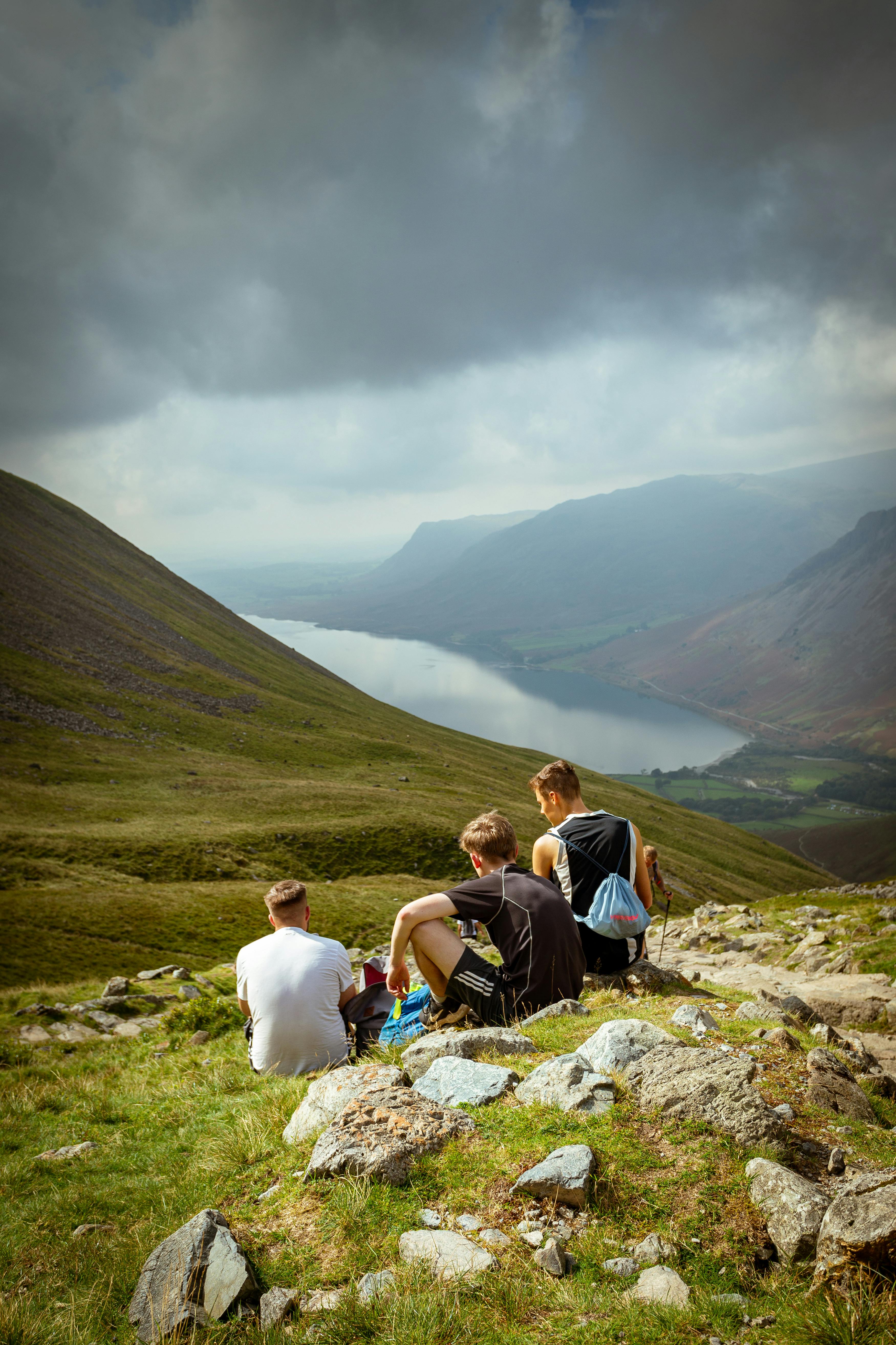 Group of hikers resting on a hillside overlooking Wasdale Valley, England, under a cloudy sky.