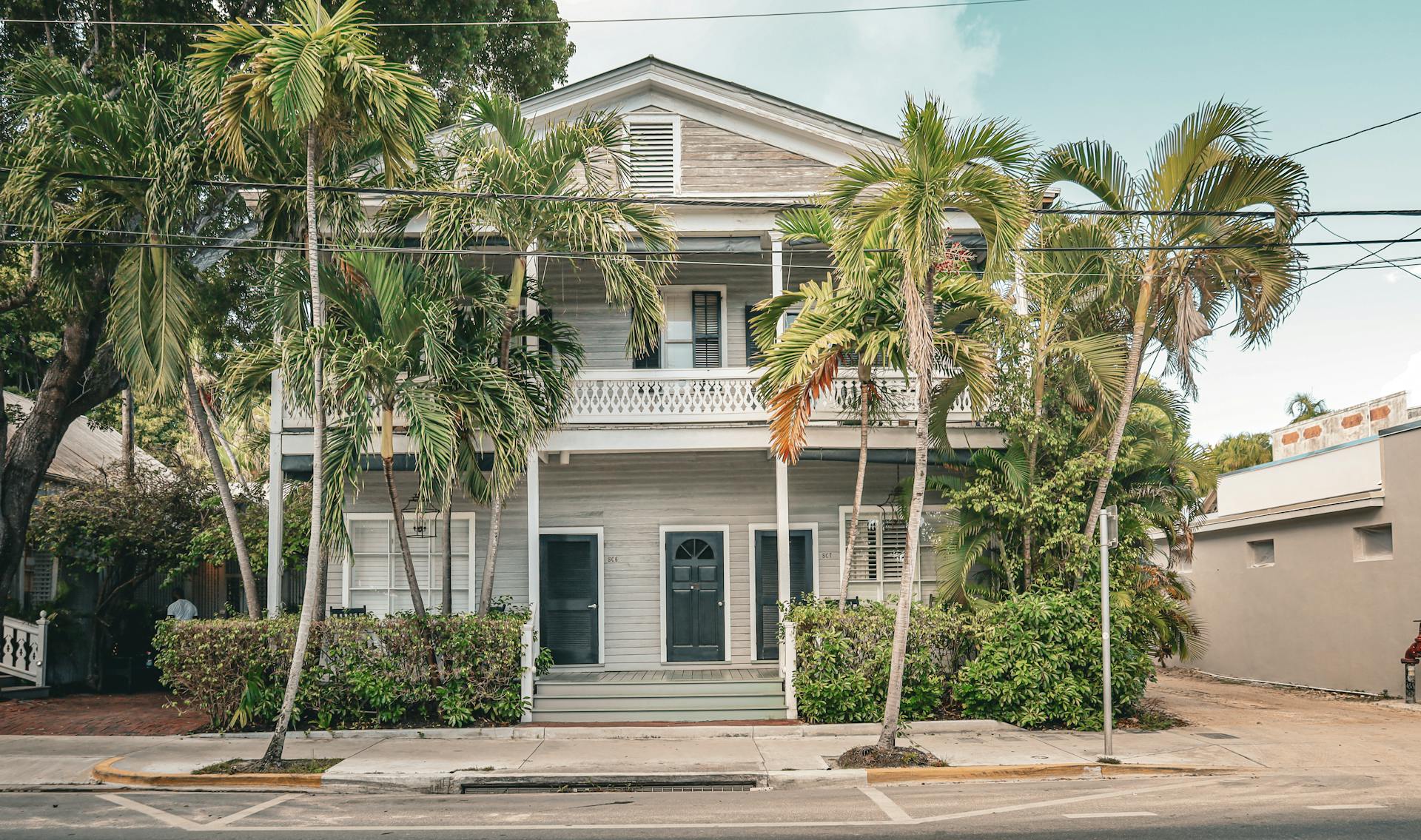 Front view of a traditional Key West house with lush palm trees, showcasing classic architecture.