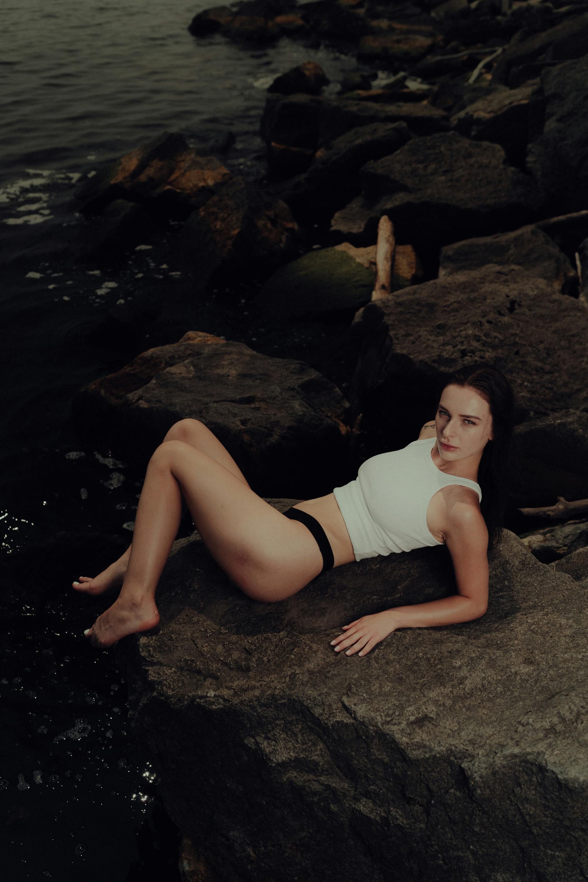 a woman laying on a rock by the water