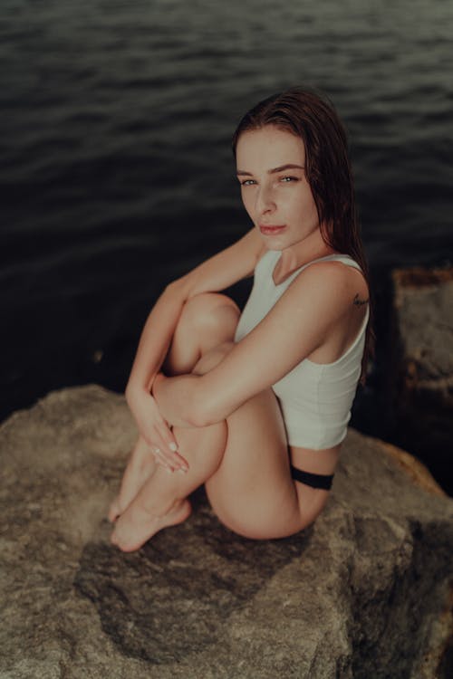 Free A woman sitting on a rock by the water Stock Photo