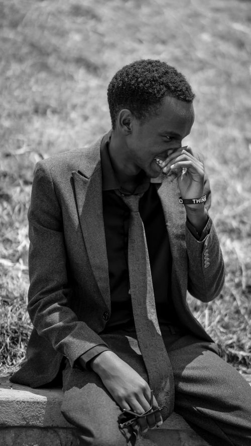 Free Black and white portrait of a smiling young man in a suit, sitting outdoors. Stock Photo