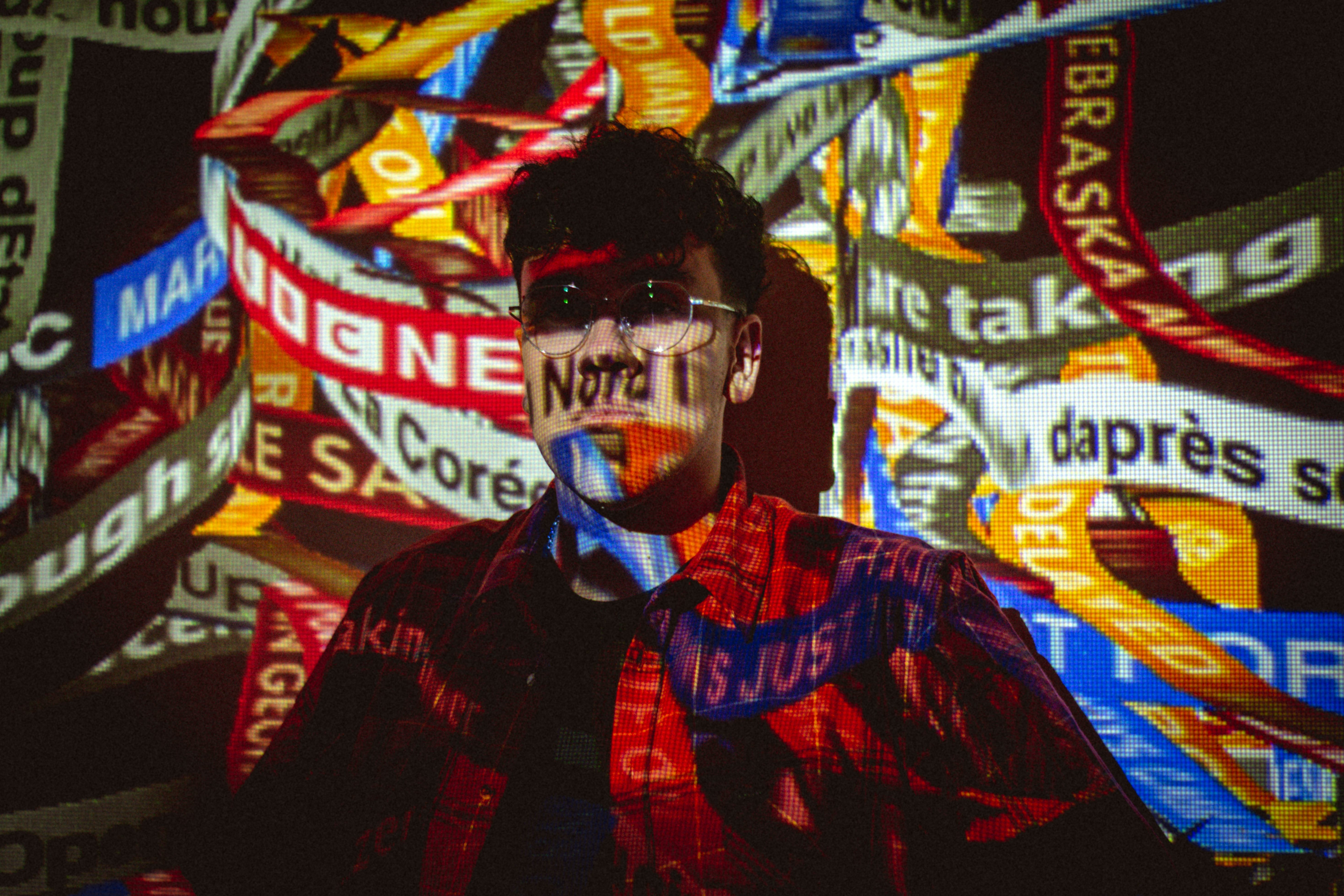 Man wearing glasses with colorful text projections on his face in a vibrant indoor setting.