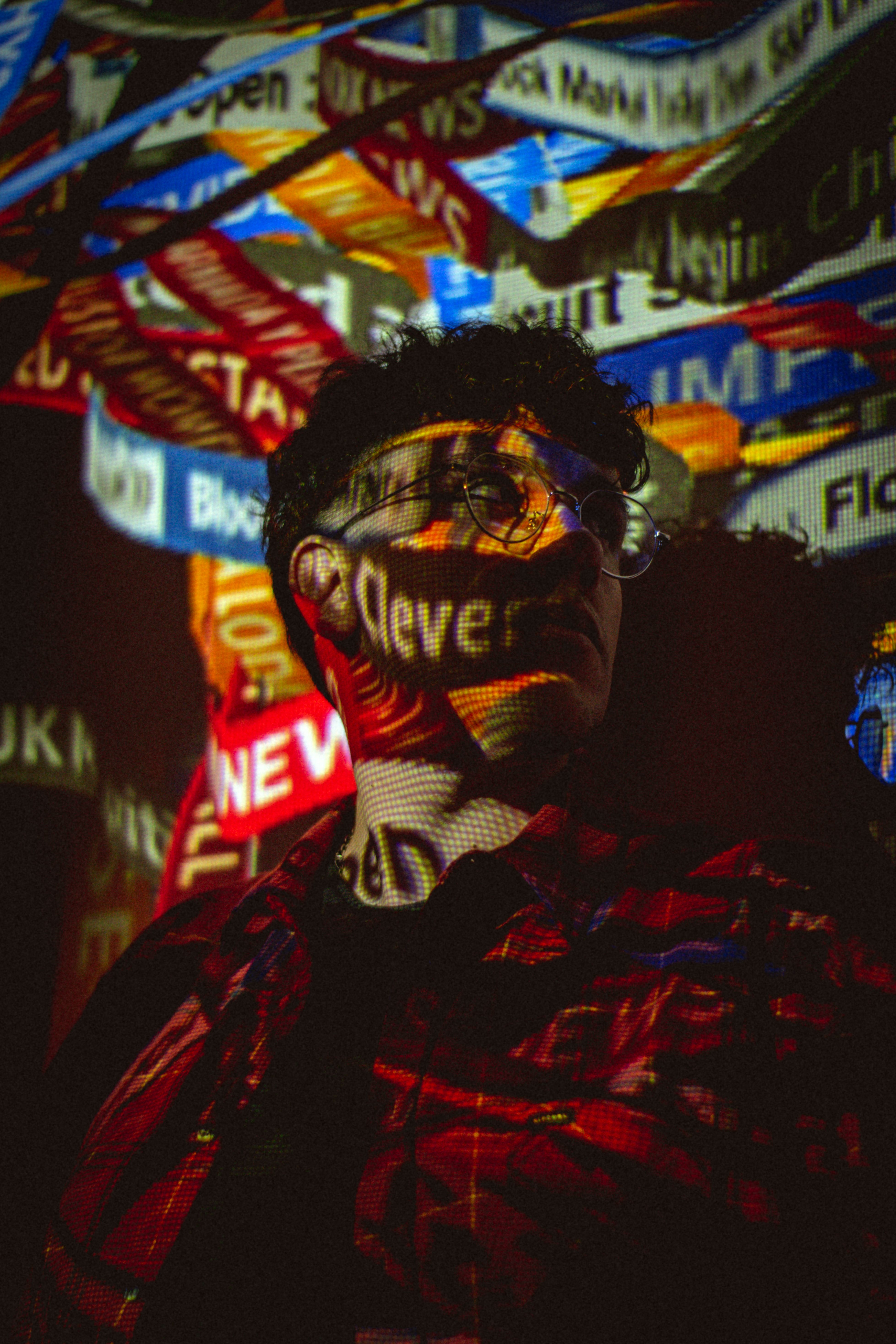 Portrait of a young man with vibrant digital text projections in a dark setting.