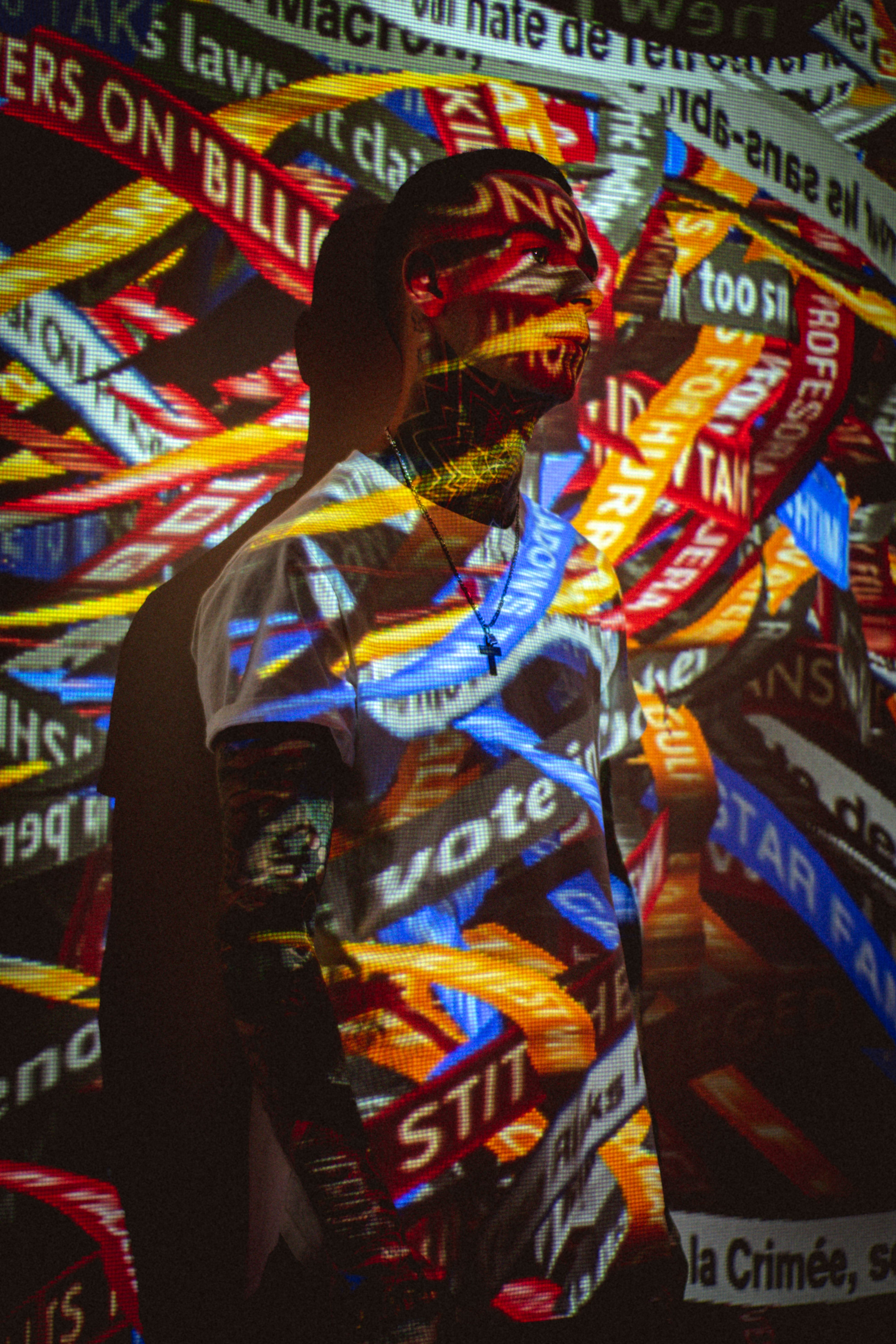 Artistic projection of vivid colors on a tattooed man standing indoors, creating a lively visual effect.