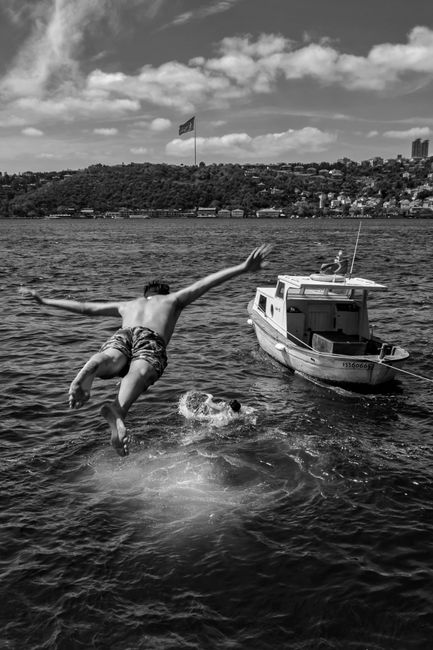 A man jumps midair from a boat into the water, showcasing summer fun.