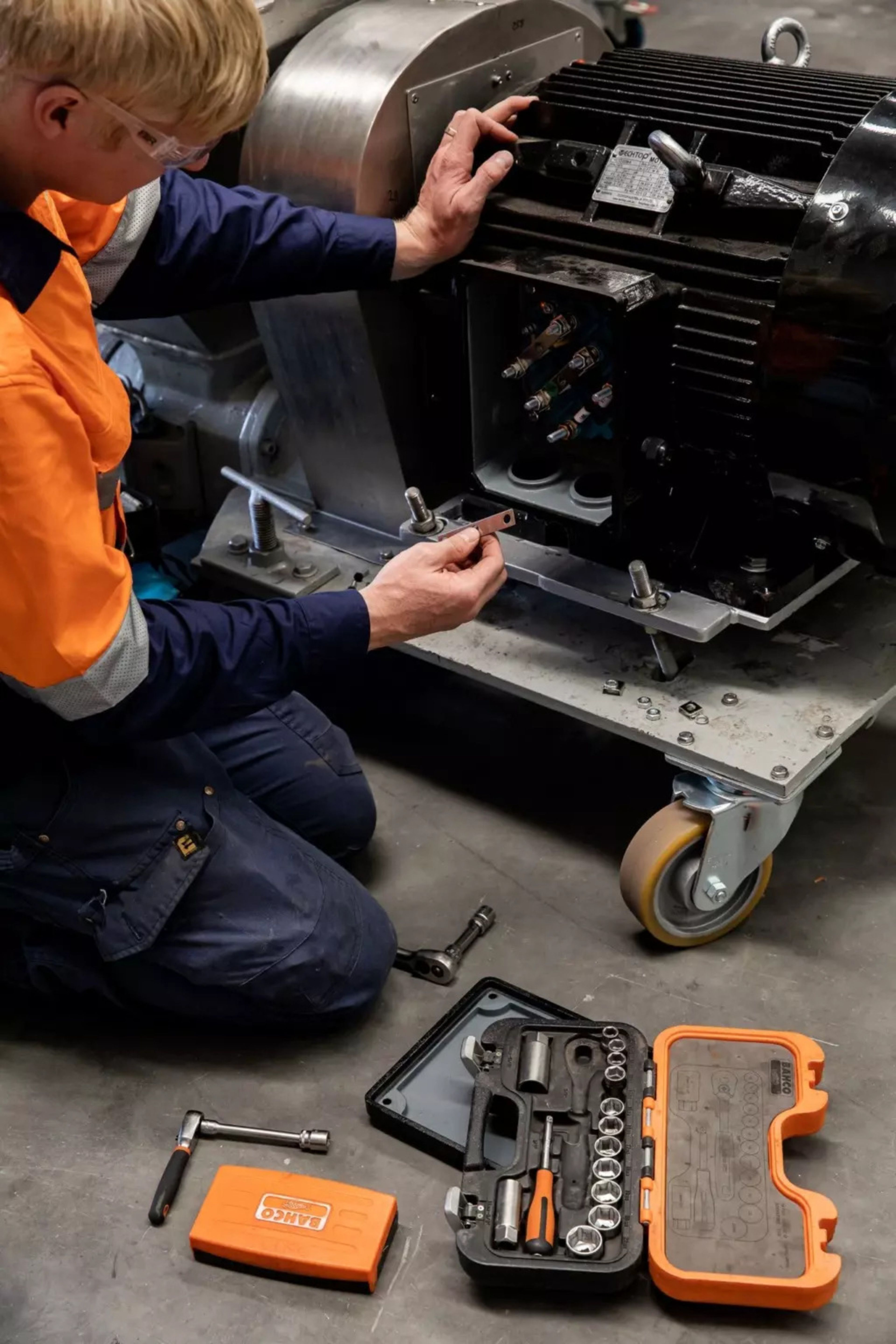 Intervenant en équipement de protection réparant une machine industrielle à l'aide de son outillage