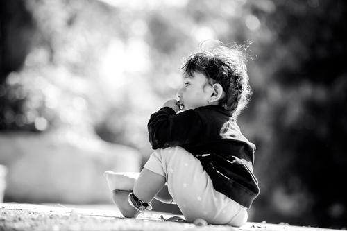Free Black and white photo of a cute child sitting outdoors in a sunlit park. Stock Photo