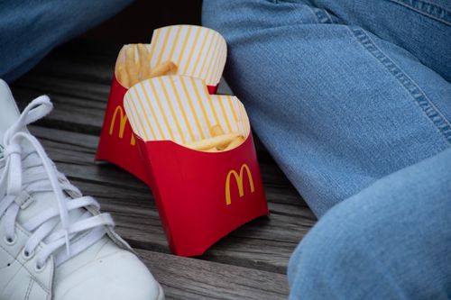 Free Two red cartons of McDonald's French fries between jeans and sneakers on a wooden surface. Stock Photo