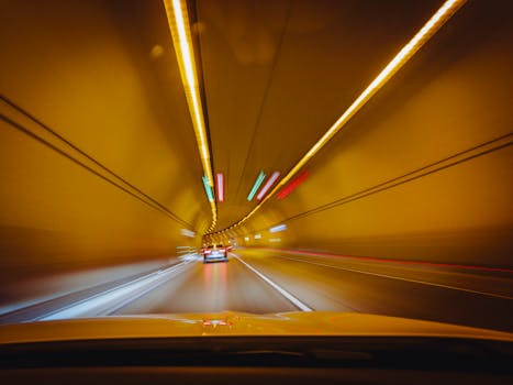 Blurry traffic scene with cars speeding through a brightly lit tunnel at night.