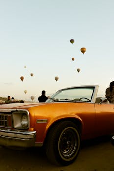 Retro car amidst hot air balloons in the skies of Cappadocia, Turkey, at sunset.
