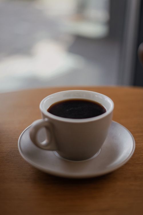 Free A close-up shot of espresso coffee in a white ceramic cup with a saucer on a wooden table. Stock Photo