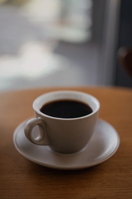 Close-up of a steaming black coffee in a white ceramic cup on a wooden table indoors.