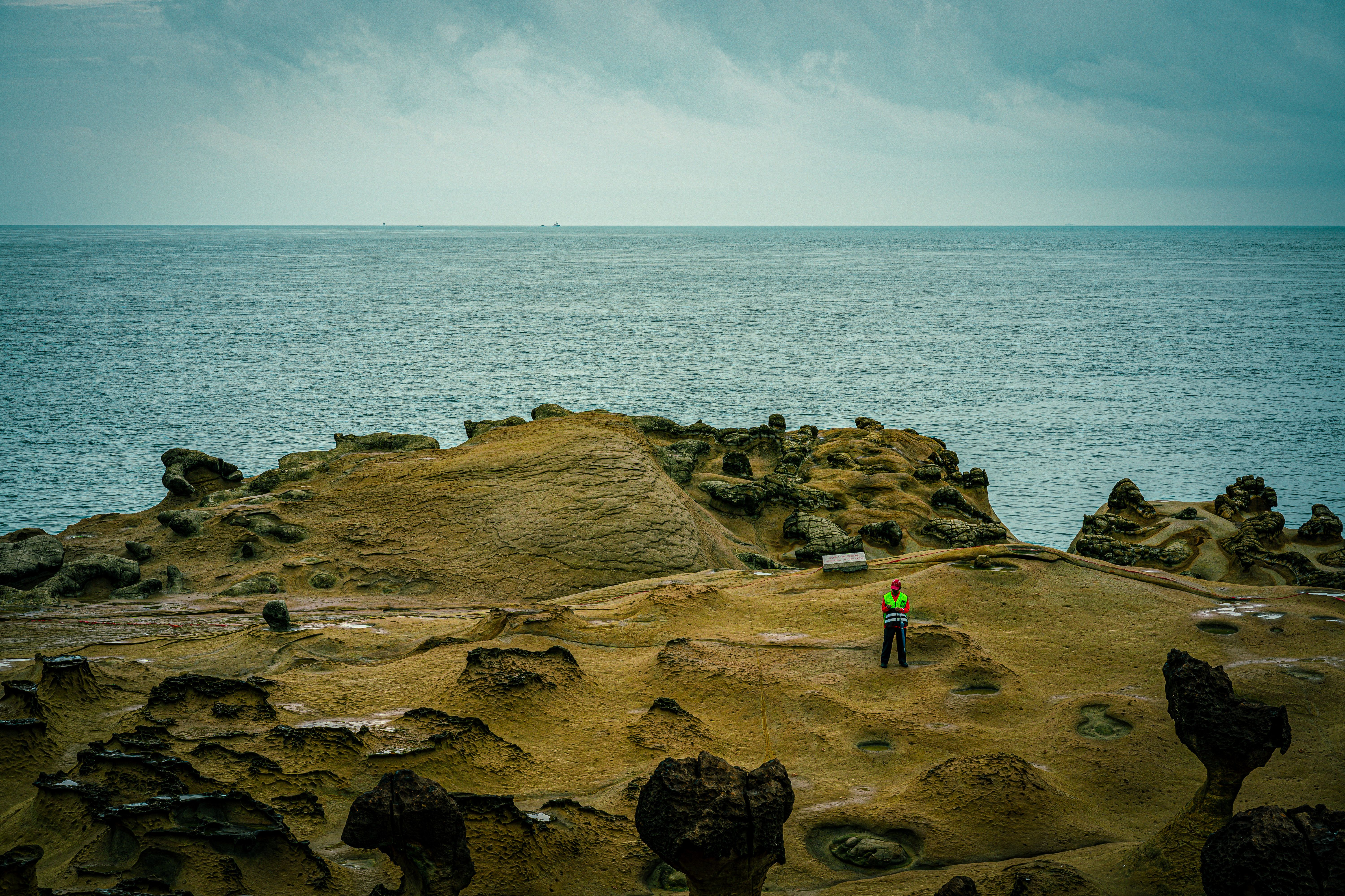 Explore the unique rock formations at Yehliu Geopark by the sea, featuring a lone person admiring the scenery.