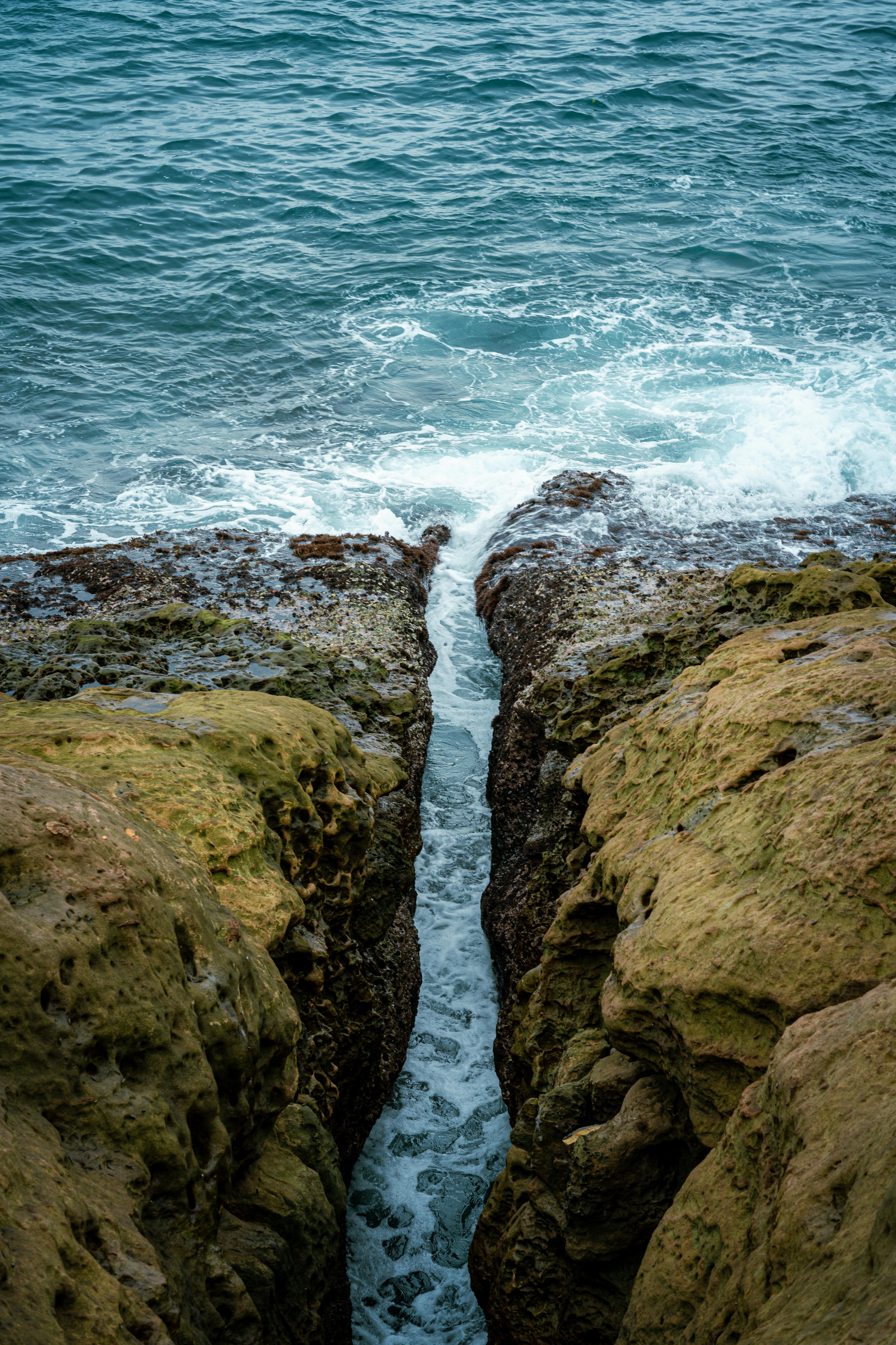 A scenic view of waves crashing against rocky cliffs on a summer day.