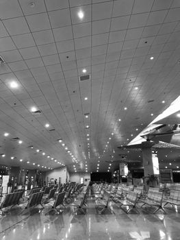 Black and white photo of an empty airport waiting room with seating and lighting.
