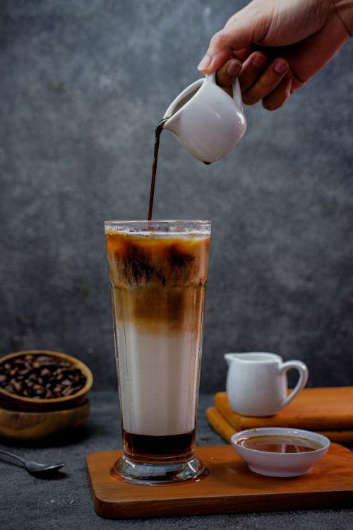 Free Close-up of hand pouring espresso into a glass of milk for iced coffee, against a textured background. Stock Photo