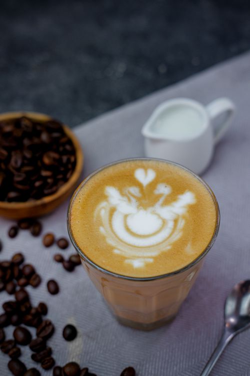 Free A detailed view of a cup of latte with artistic foam, surrounded by coffee beans and milk jug. Stock Photo