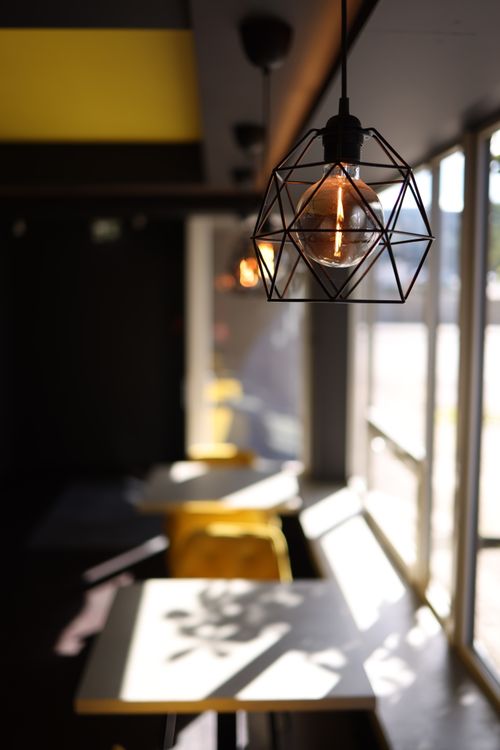 Free A modern café with geometric light fixtures and sunlit tables, creating a cozy atmosphere. Stock Photo