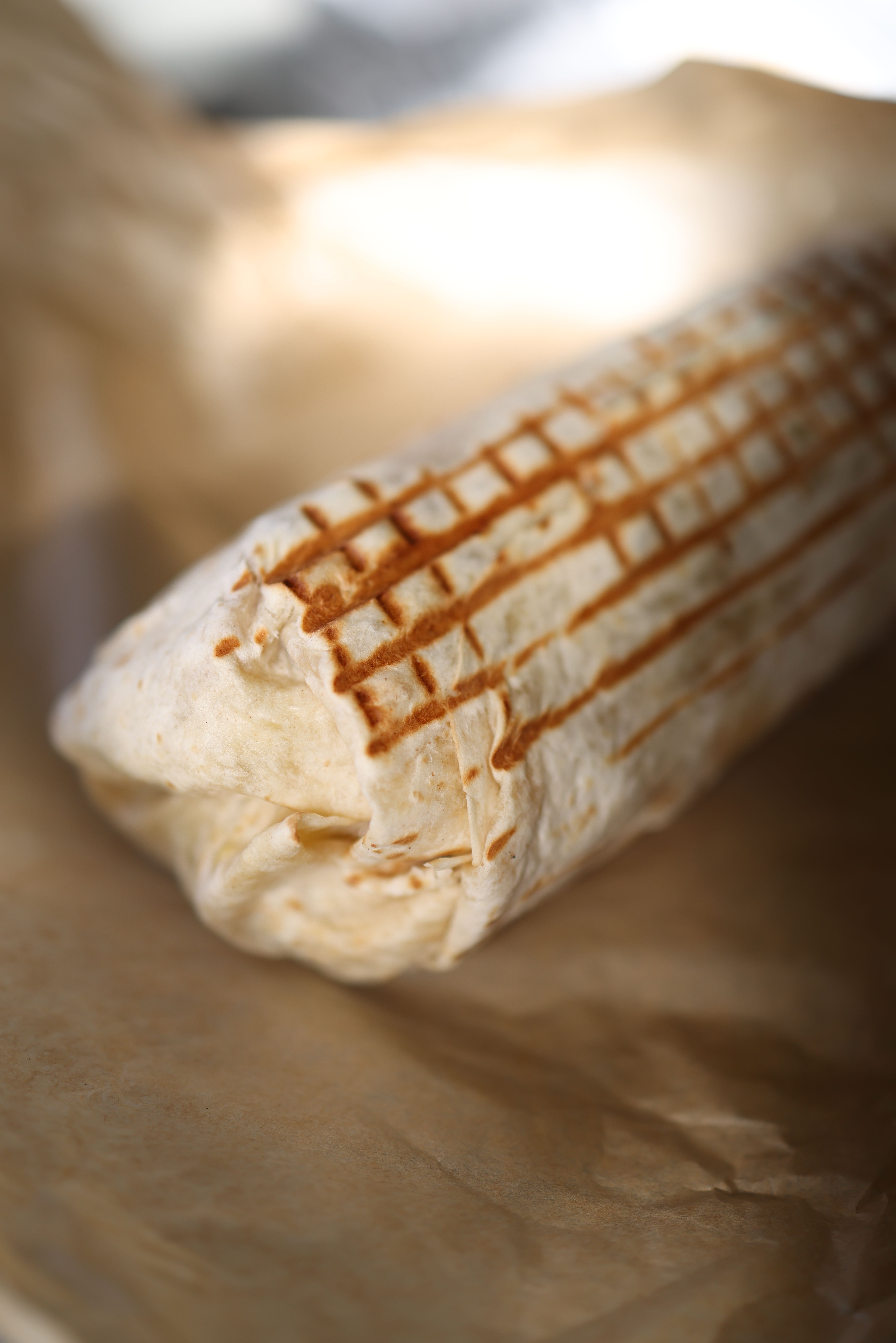 Close-up of a freshly grilled burrito wrapped in brown paper, showcasing its texture.