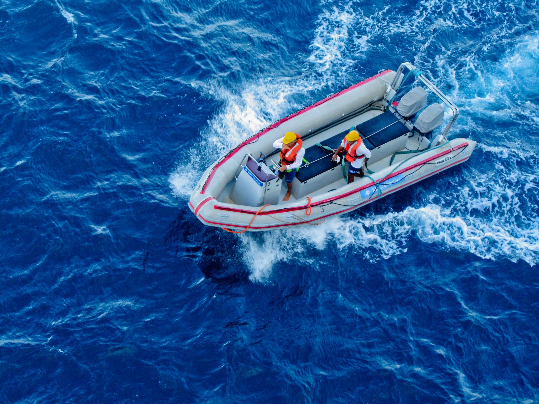 Two people in a motorboat navigating the ocean, captured from above.