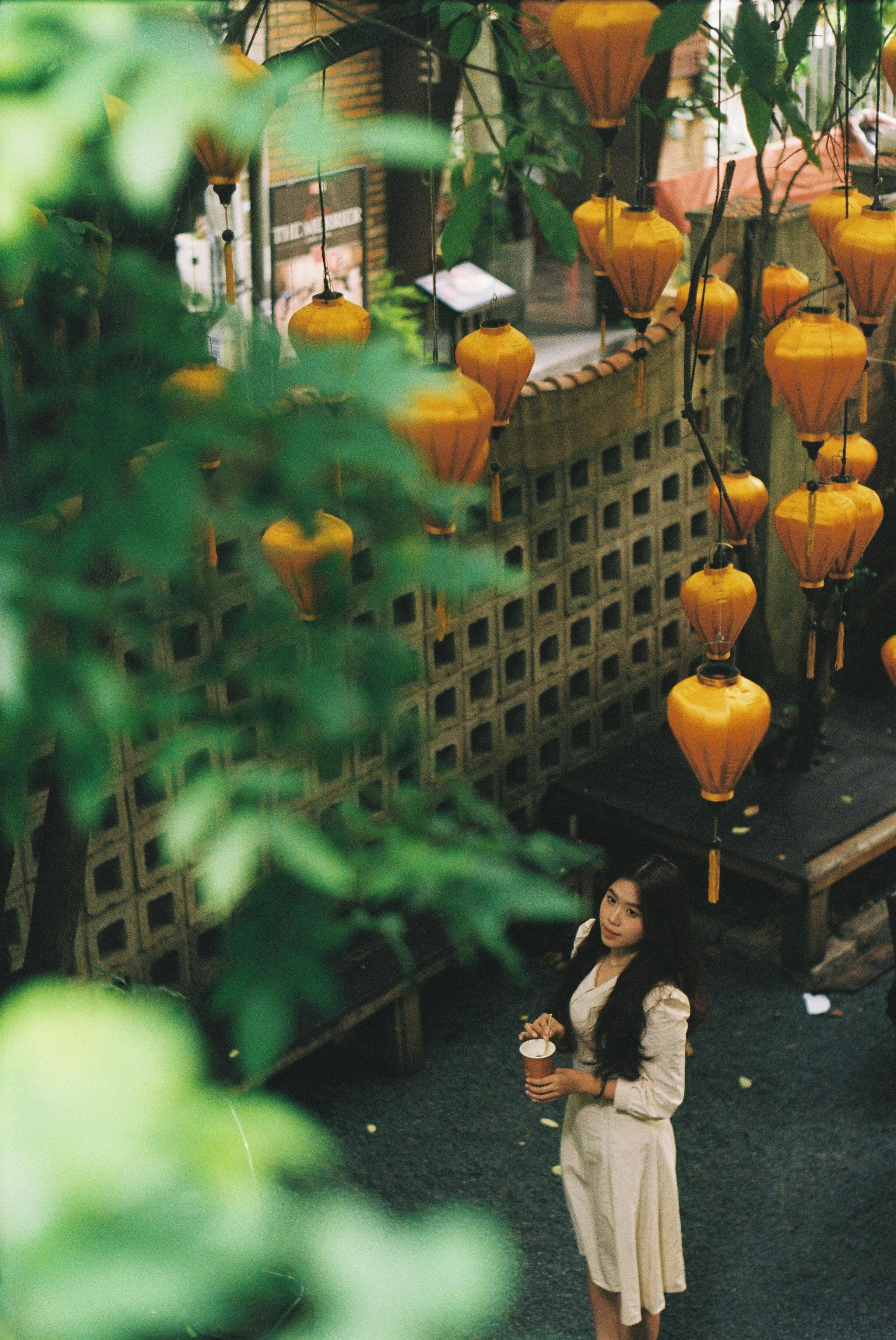 A woman stands in an urban setting adorned with hanging decorative lanterns, captured from above.