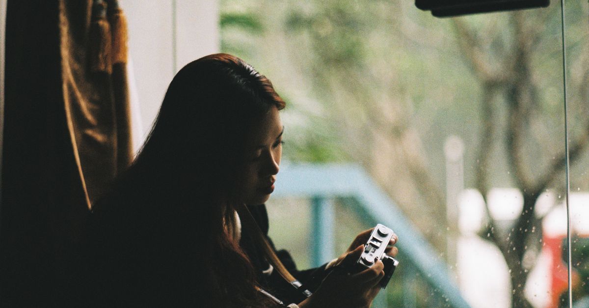 A person sitting by a window, looking thoughtfully at the rain, with a phone face-down on the table