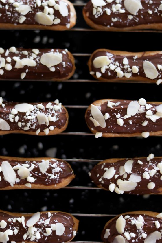 Rows of eclairs coated in chocolate glaze with sliced and chopped almonds on a cooling rack