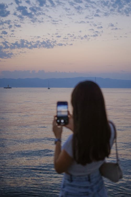 A woman taking a photo of the ocean with her cell phone