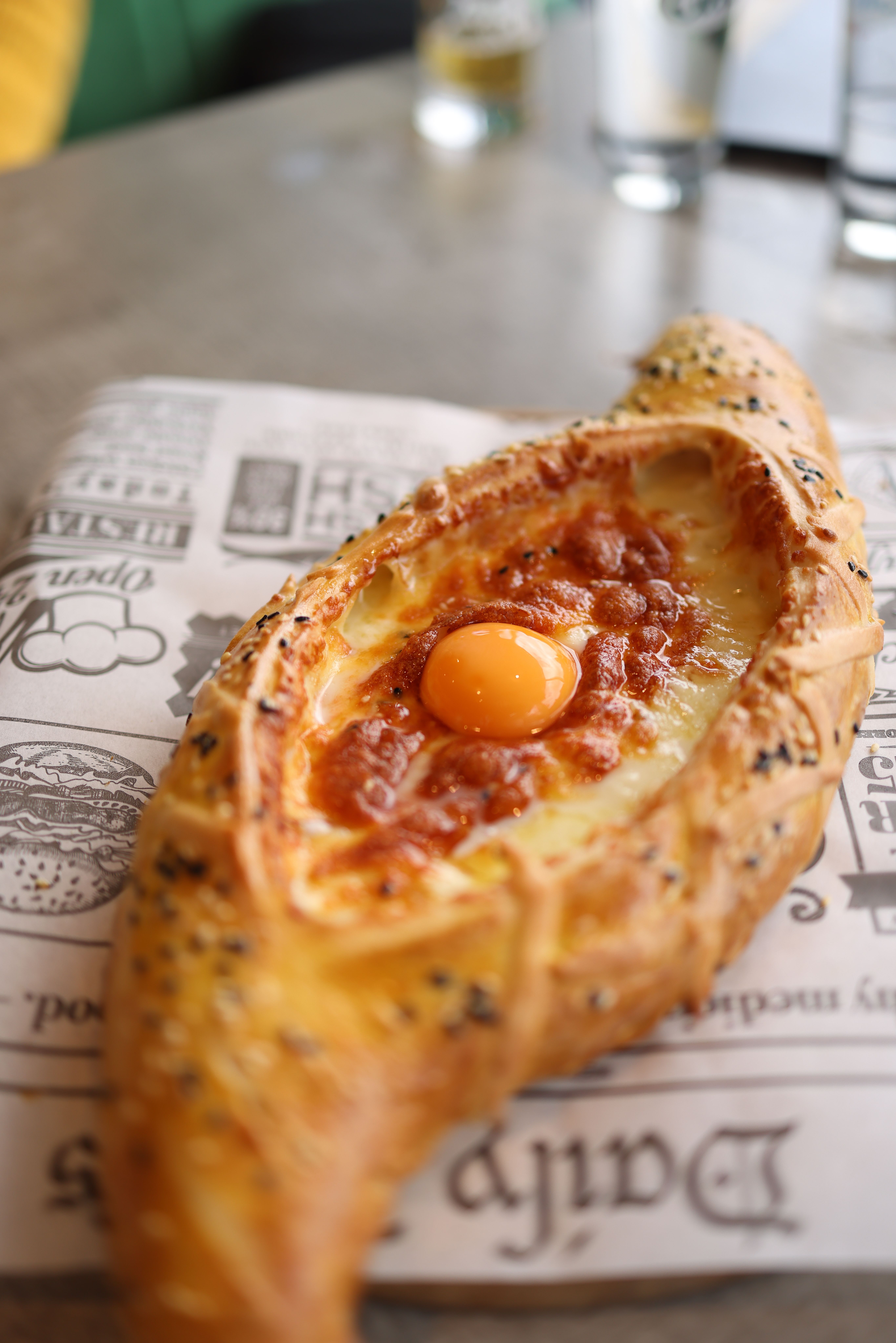 Close-up of Georgian khachapuri topped with egg yolk on rustic paper.