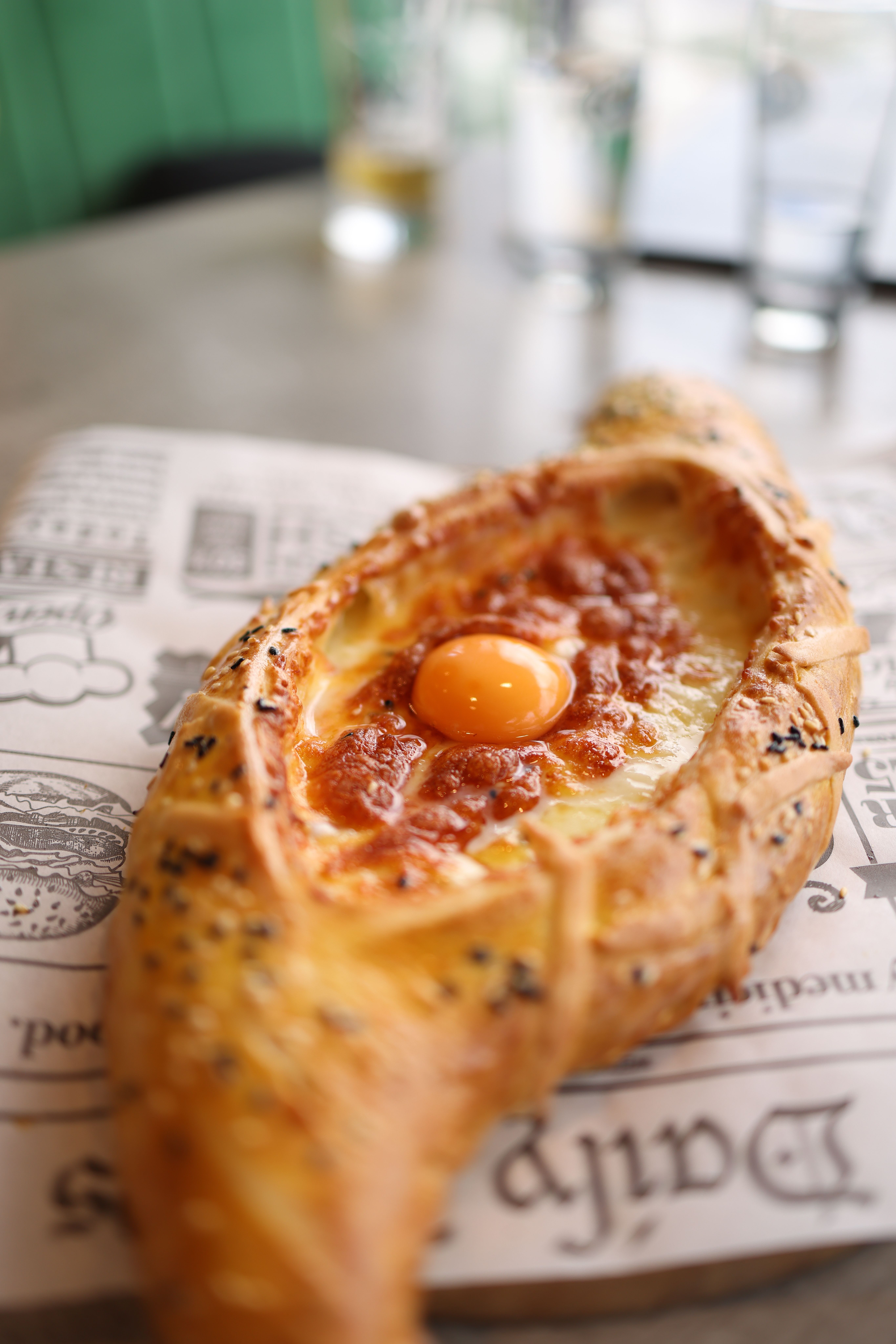 Delicious Adjarian khachapuri filled with cheese and topped with a fresh egg yolk, served on decorative paper.