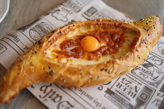 Delicious Georgian khachapuri topped with a golden egg yolk and melted cheese on a patterned paper.