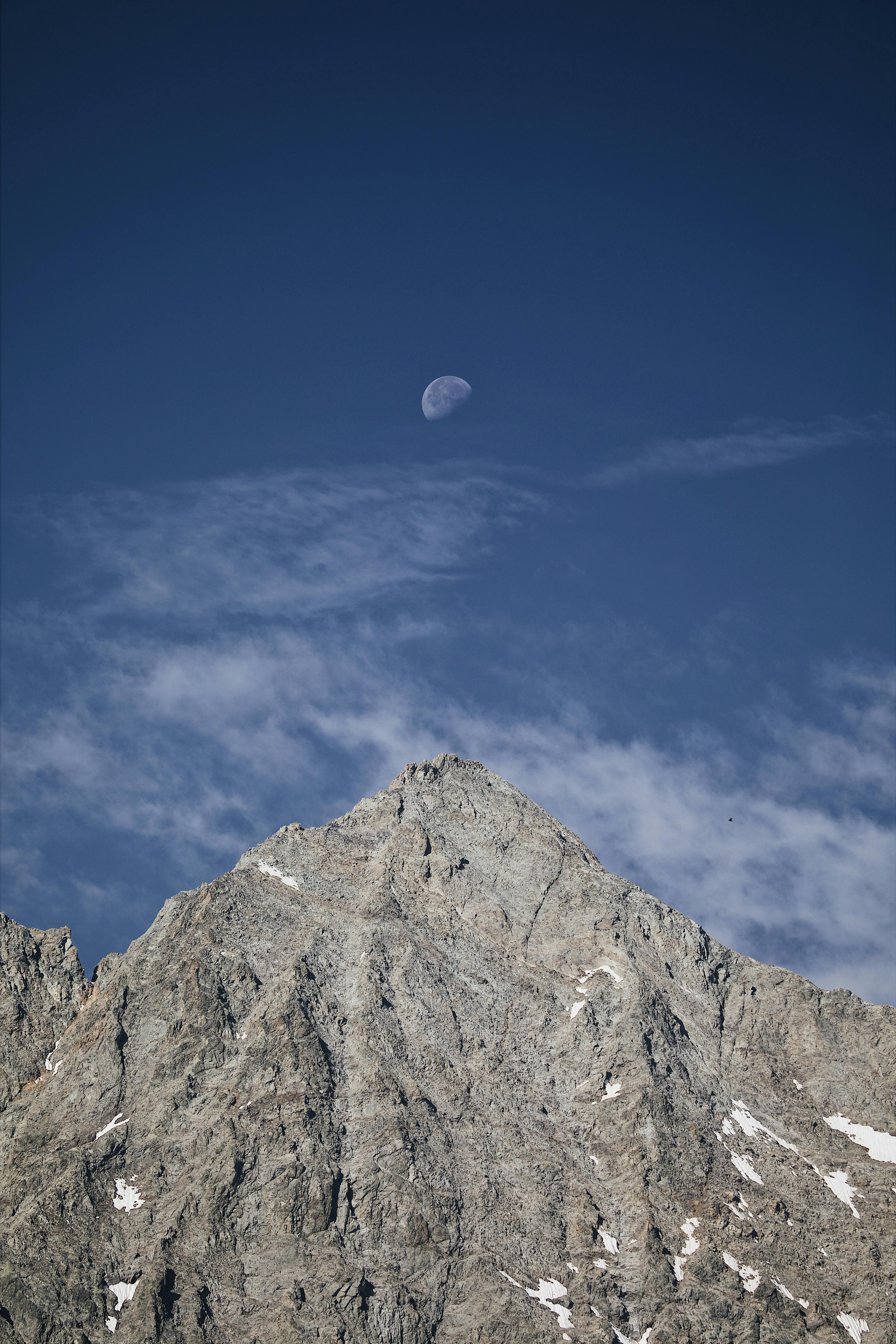 Stunning mountain peak with a visible moon, captured under a clear blue sky.