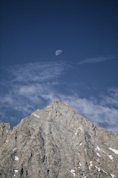 Stunning mountain peak with a visible moon, captured under a clear blue sky.
