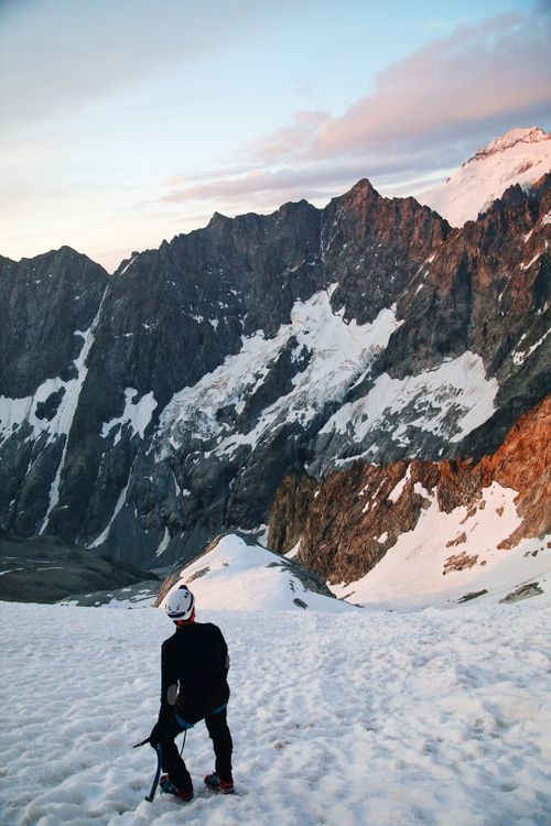 Free Climber prepares to scale snow-covered mountain at sunrise, a scene of adventure and exploration. Stock Photo