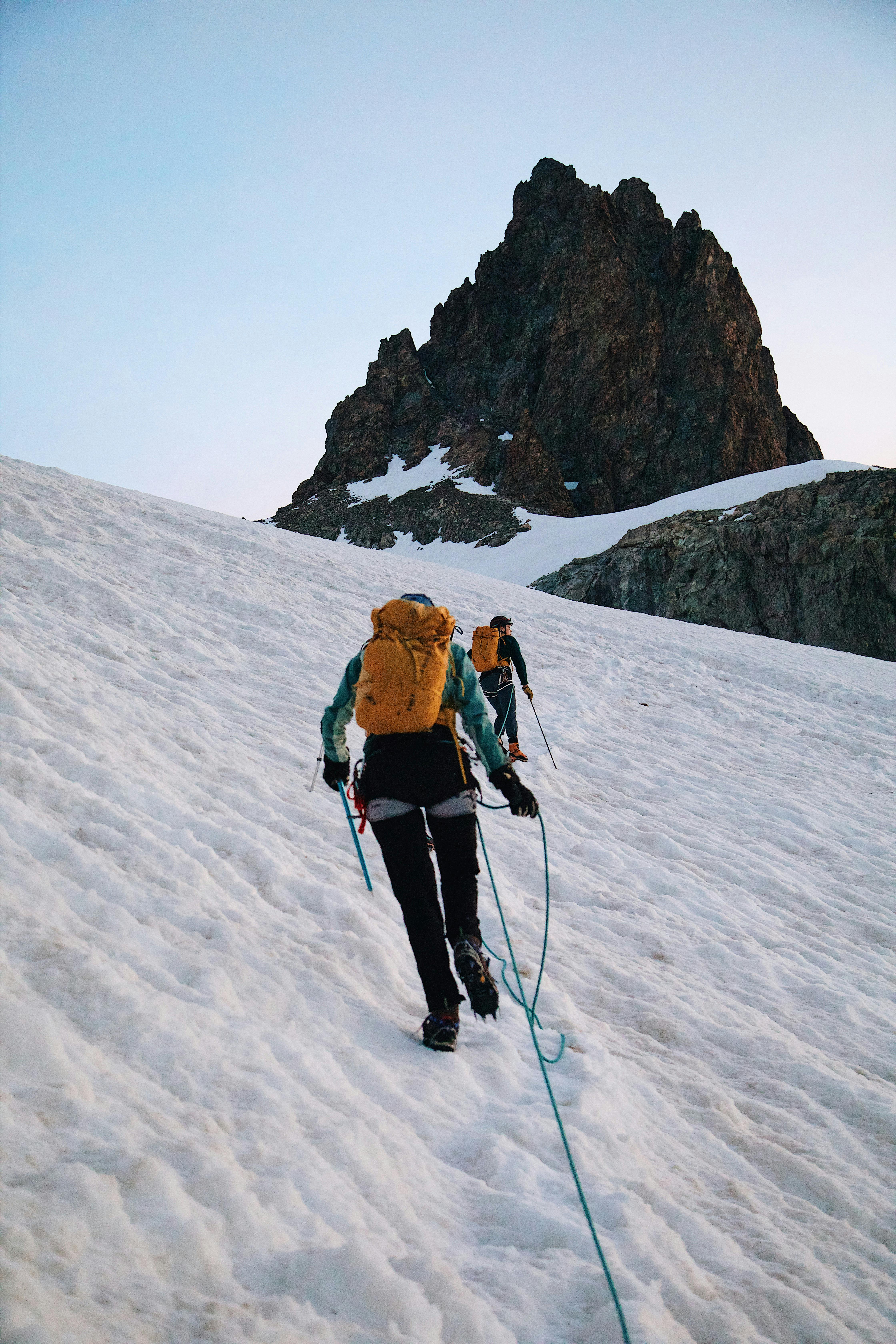 Two climbers trekking up a snowy mountain slope with gear, showcasing adventure and winter exploration.