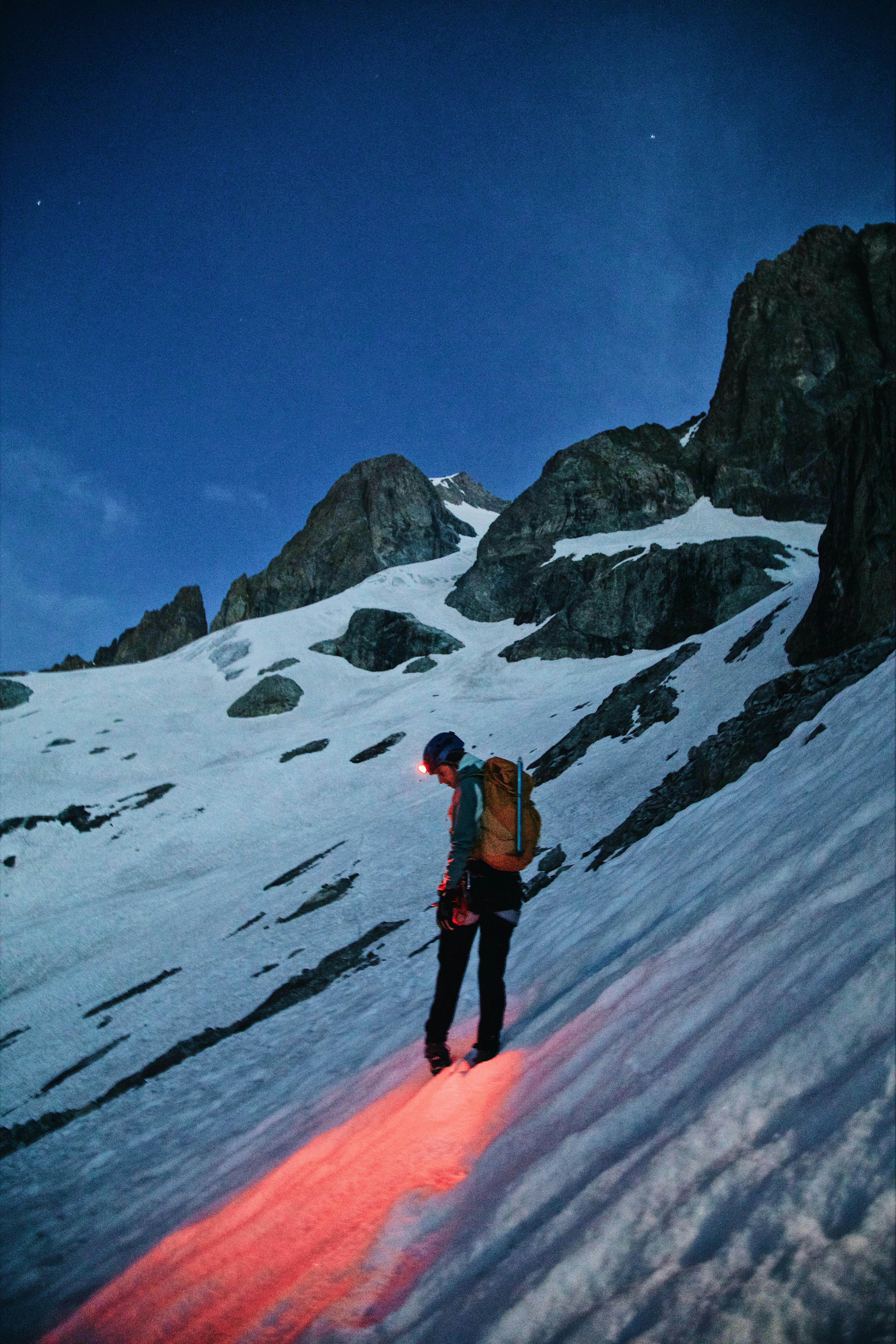 A lone climber explores a snowy mountain under a starry night sky, showcasing adventure.