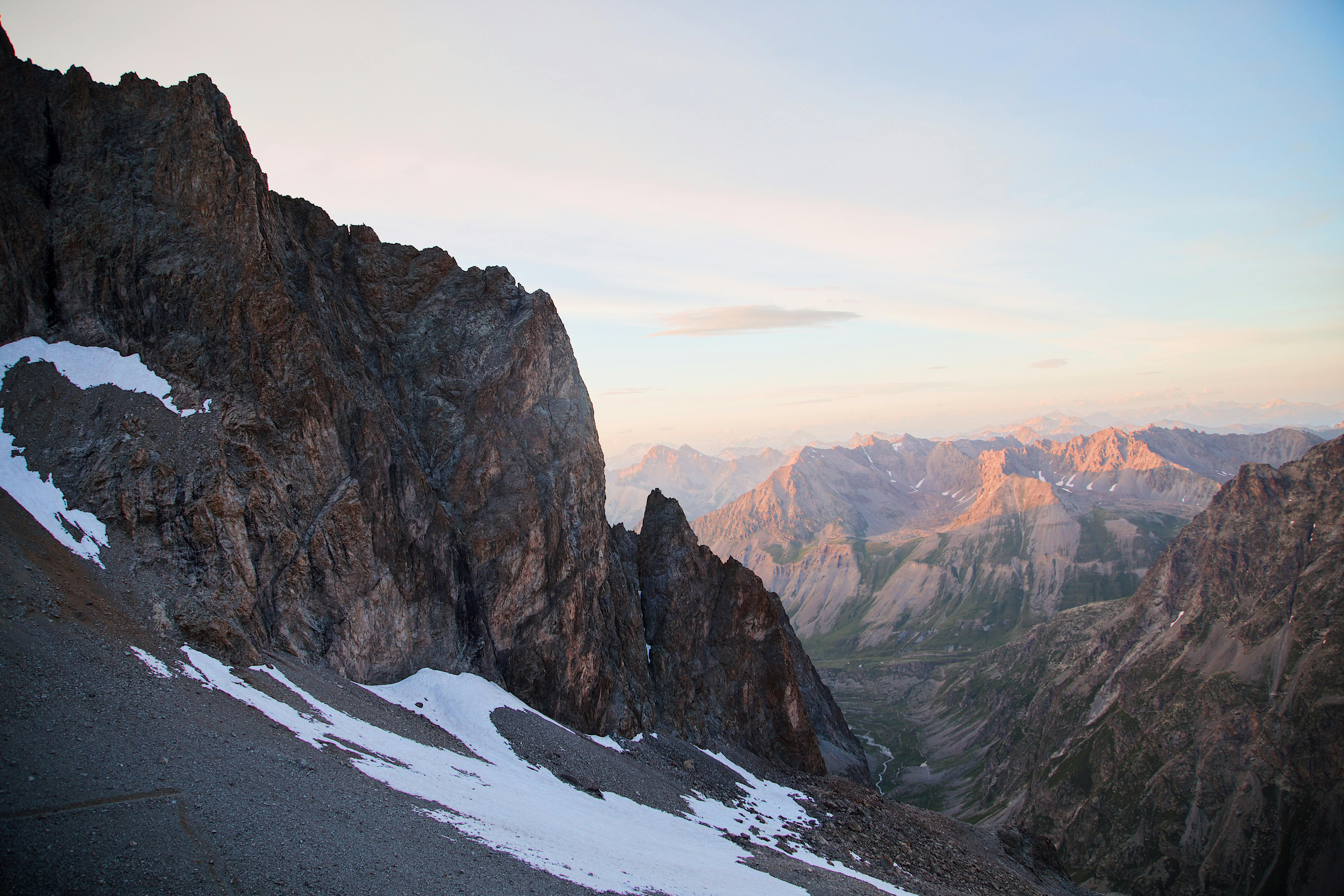Stunning view of a rocky mountain range at sunset with patches of snow and clear skies.