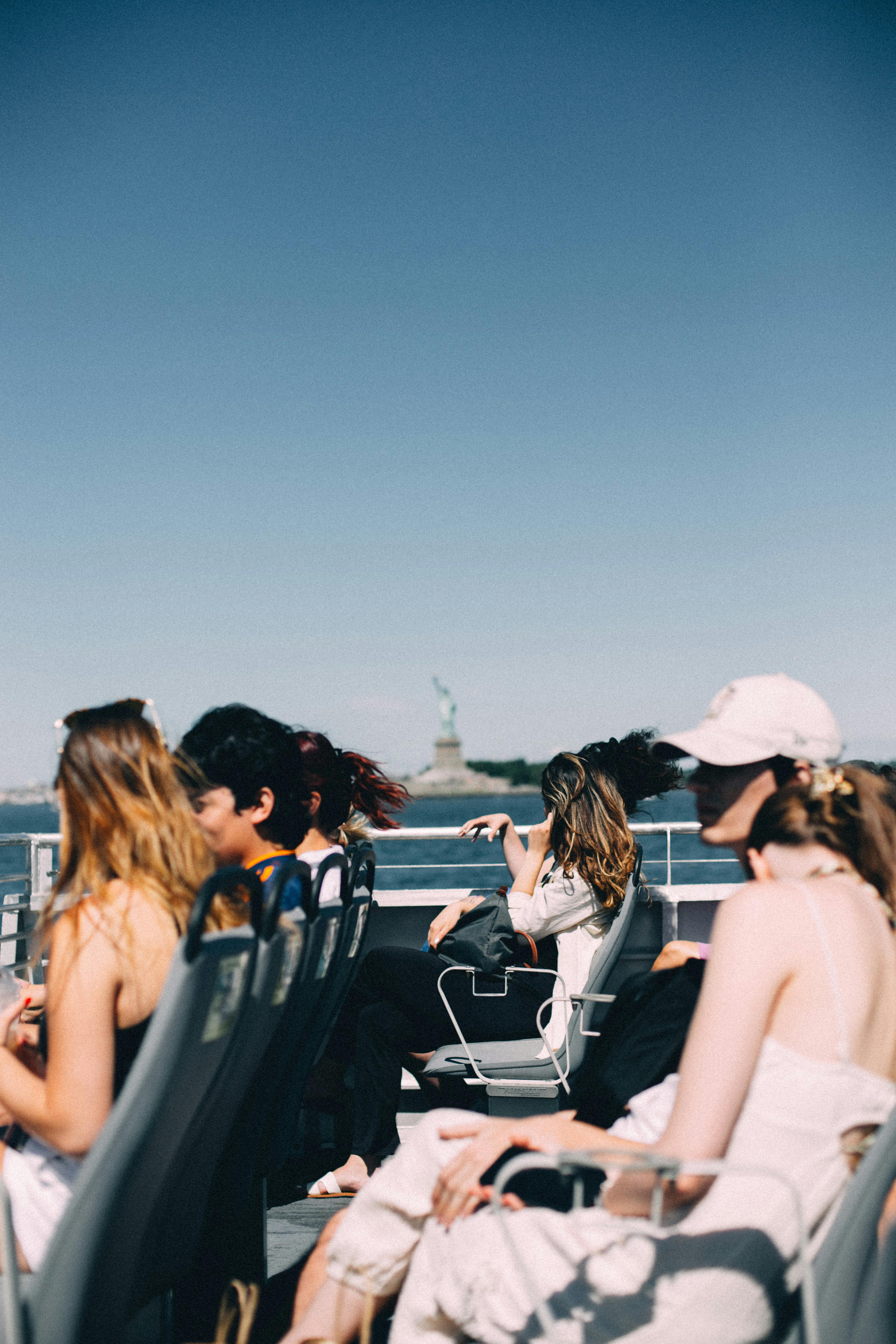 Group of tourists enjoying a sunny ferry ride towards the Statue of Liberty in New York City.