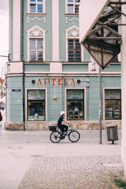 A man rides a bicycle past a historic building in Wroclaw, Poland on a city street.