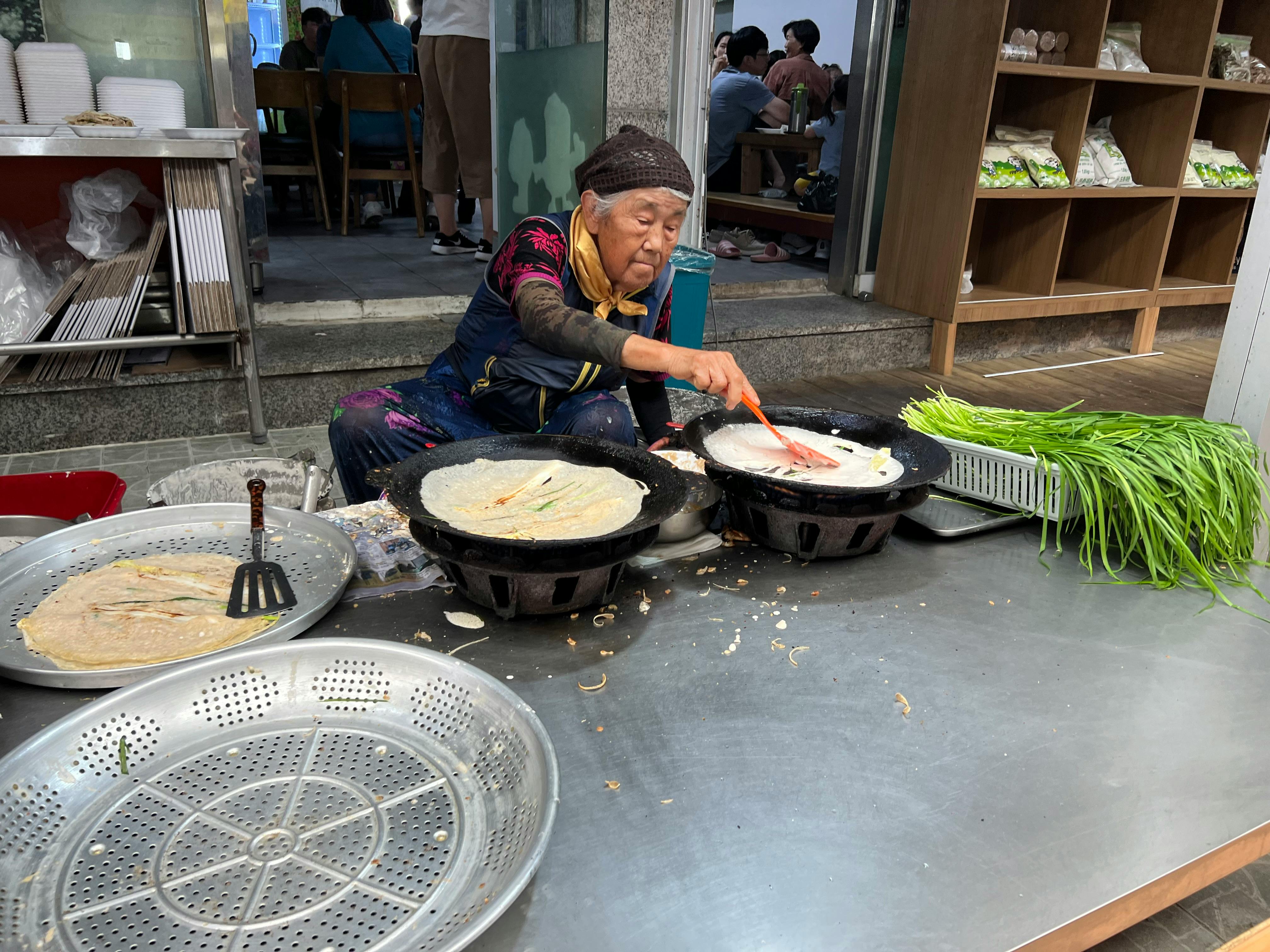 Senior woman preparing traditional pancakes on outdoor street market stall.
