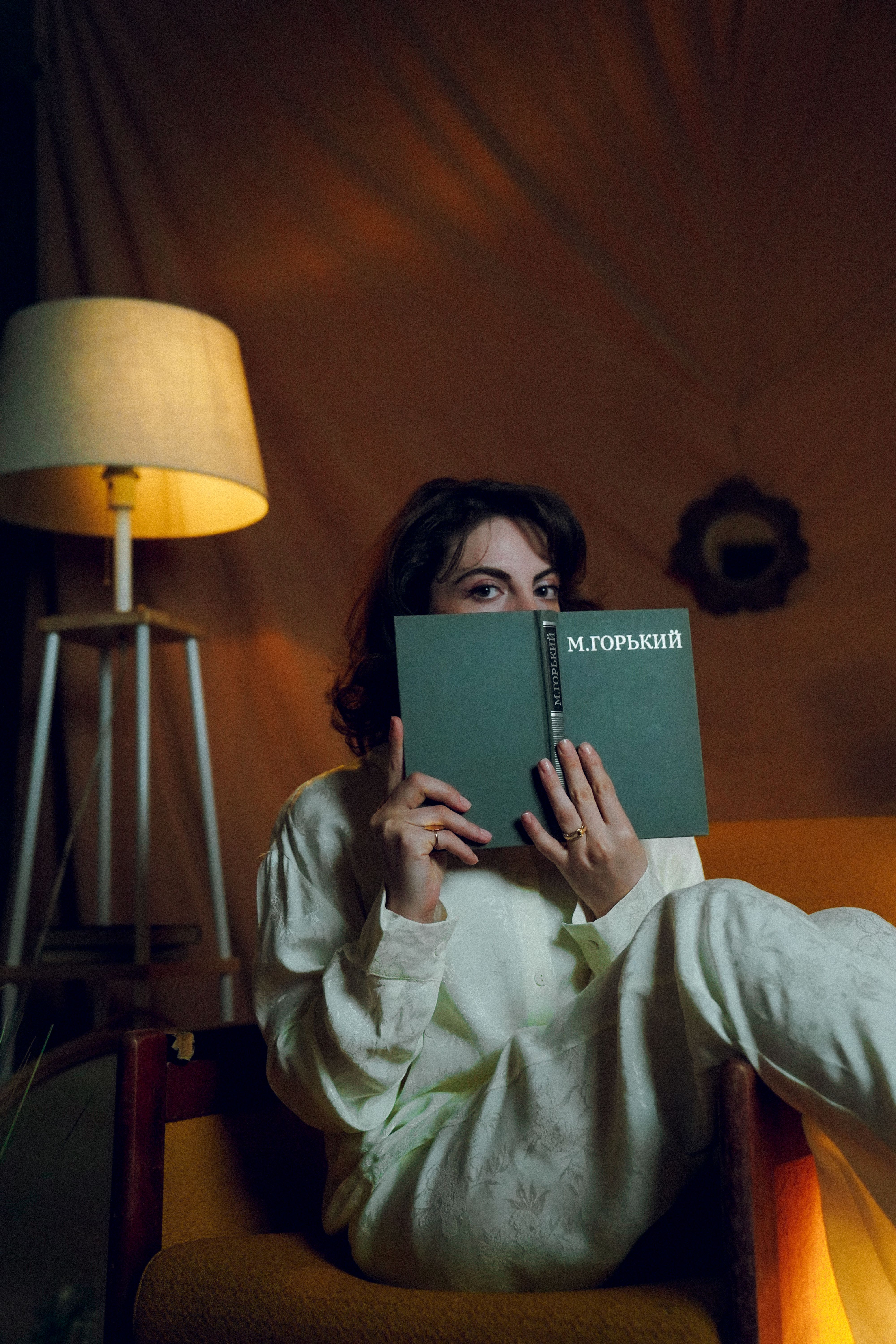 Young woman in pajamas reading a book in a cozy, vintage room in Baku, Azerbaijan.
