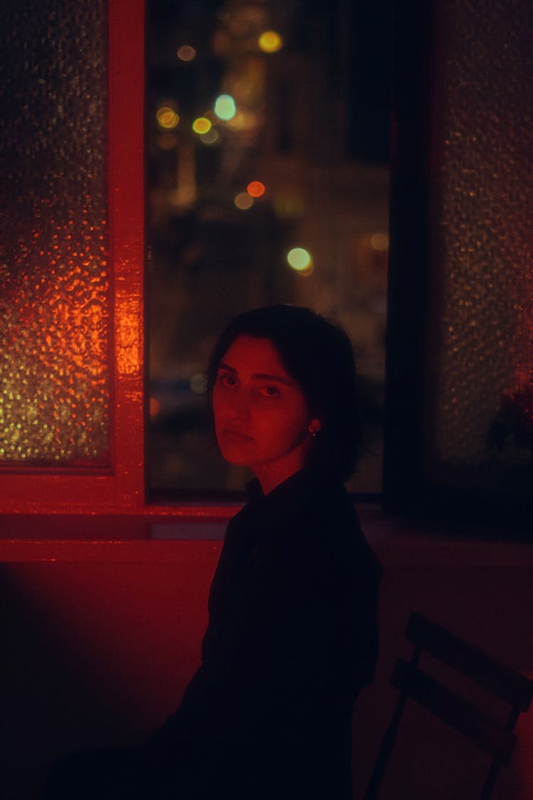 Young Brunette Woman Sitting By An Open Window At Night