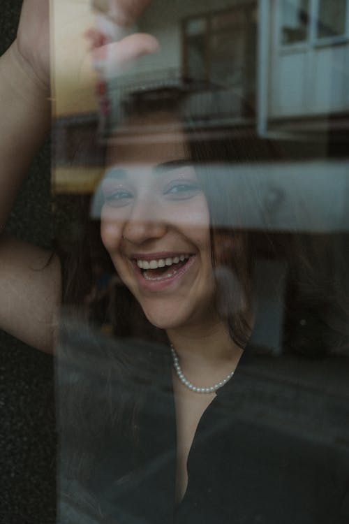 Photo of a Young Smiling Woman Standing behind the Window