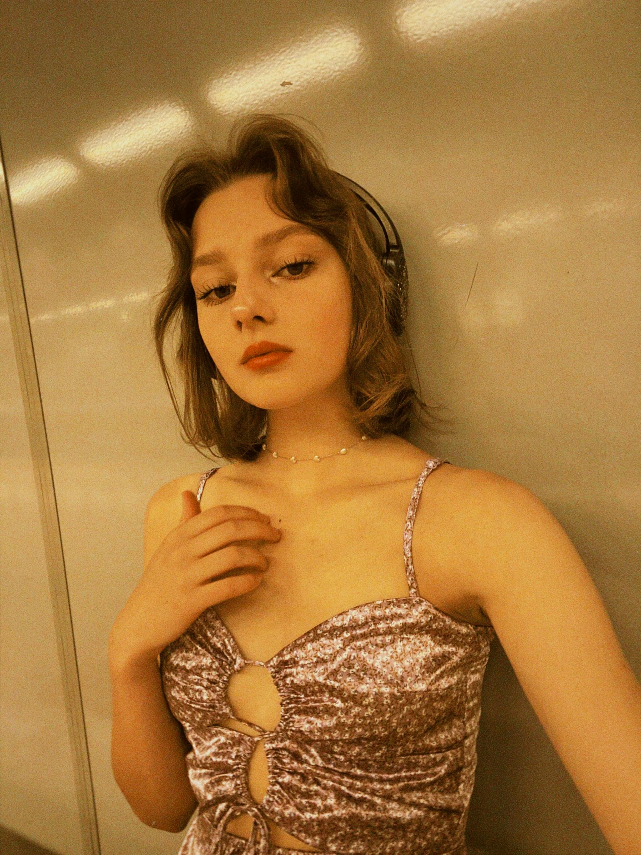 Portrait of a fashionable young woman in a metallic top with headphones, standing indoors.
