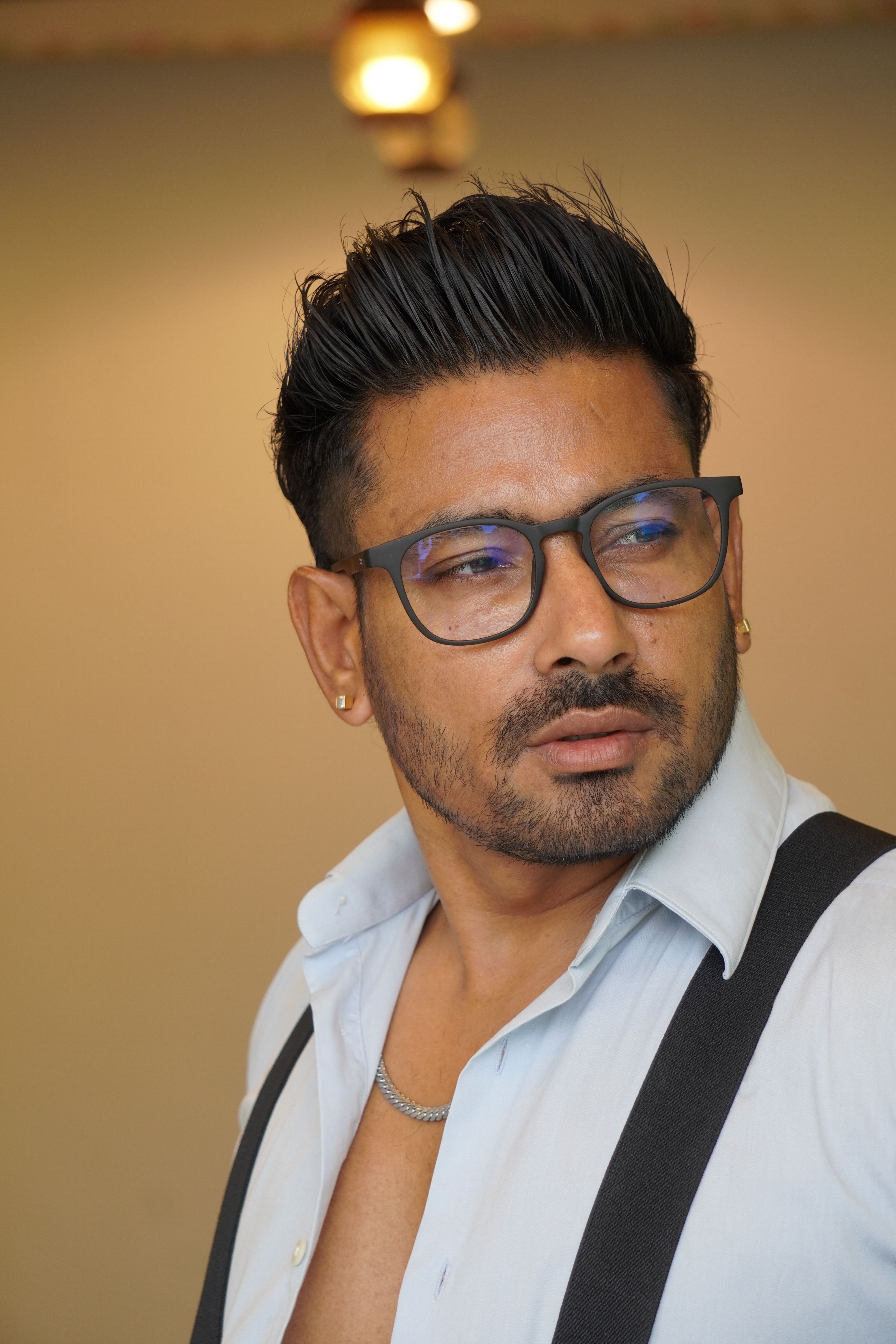 Portrait of a stylish man wearing eyeglasses and suspenders, looking thoughtfully to the side.