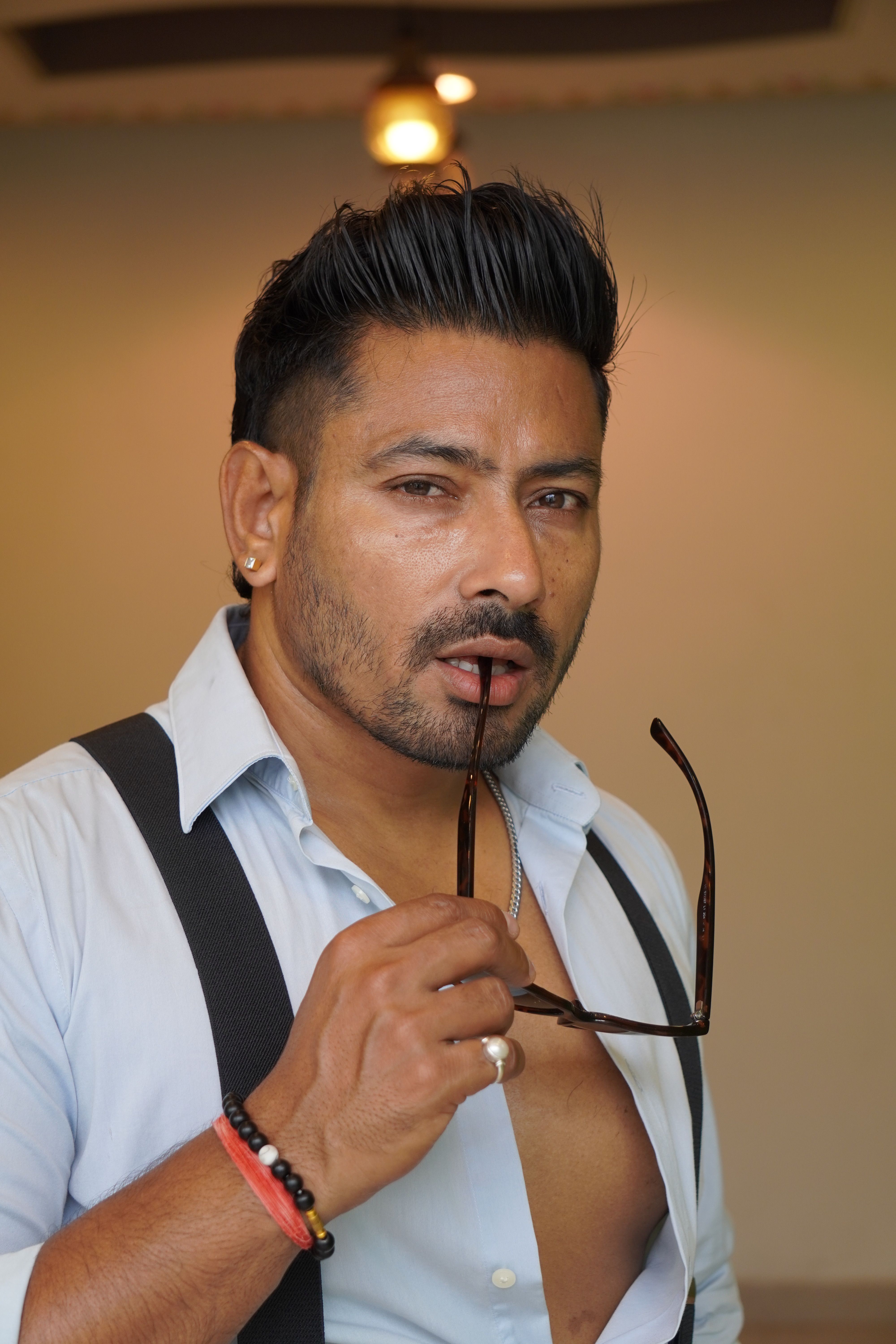 Portrait of a confident man indoors holding sunglasses, exhibiting modern style.