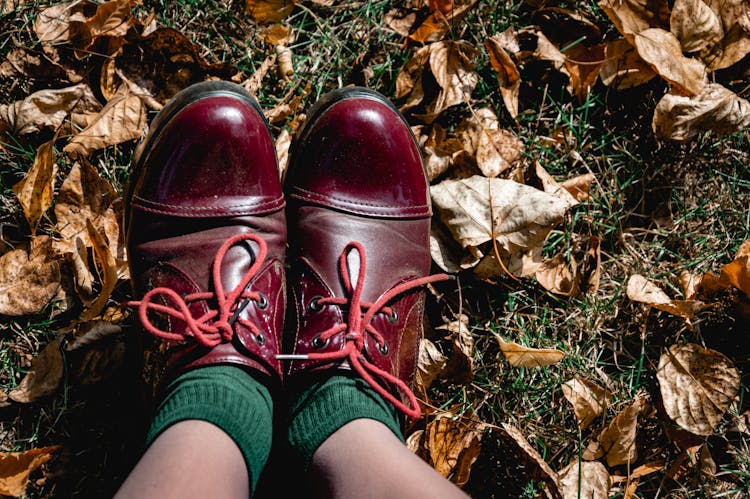 Feet In Red Leather Shoes And Green Socks On Grass With Autumnal Leaves